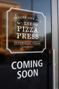 the pizza press coming soon written on a glass door